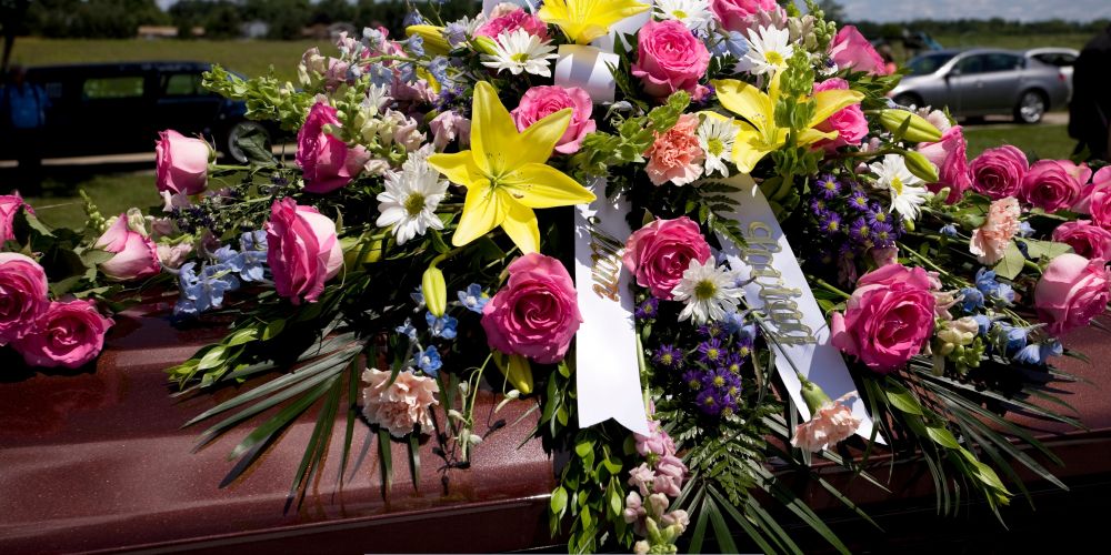 Colorful floral spray with pink roses and yellow lilies displayed on a casket at a graveside service by Funeral Home and Cremations in Waukesha, WI.