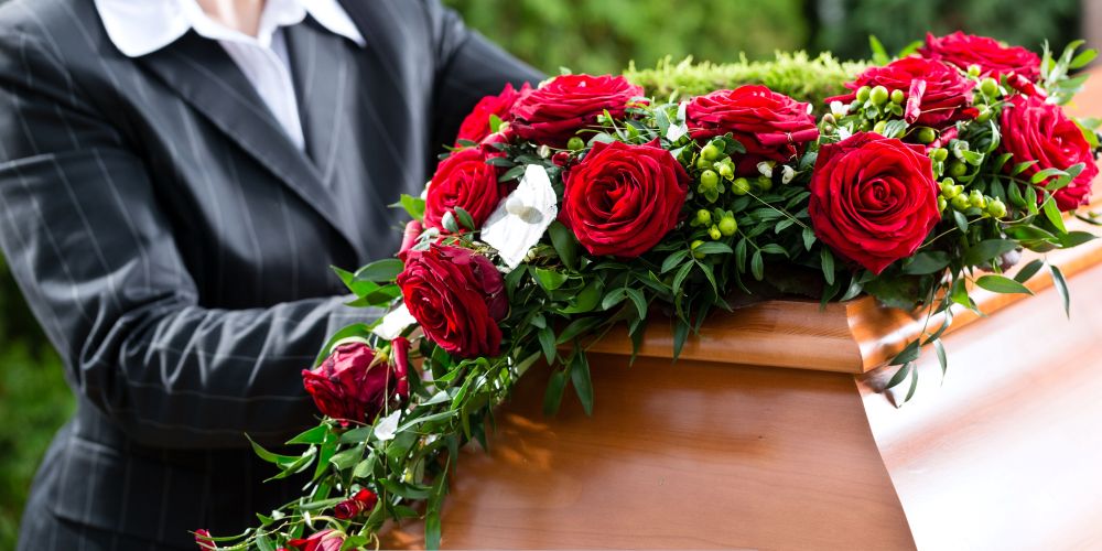 Funeral director placing a red rose arrangement on a wooden casket at Funeral Home and Cremations in Waukesha, WI.