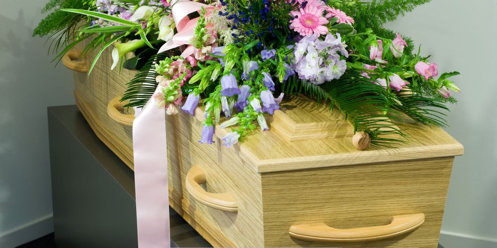 Light wood casket adorned with a colorful floral arrangement at a Funeral Home and Cremations in Muskego, WI.