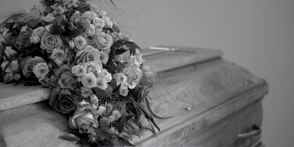 Black and white image of a casket adorned with a large rose arrangement at a Funeral Home and Cremations in West Allis, WI.
