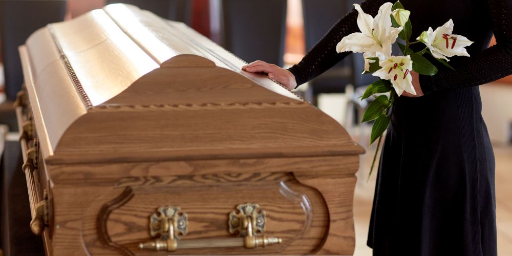 Mourner holding white lilies while standing beside a wooden casket at a Funeral Home and Cremations in West Allis, WI.