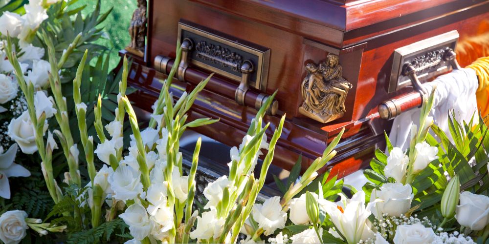 Polished wooden casket surrounded by white floral arrangements at a Funeral Home and Cremations in West Allis, WI during a graveside service.