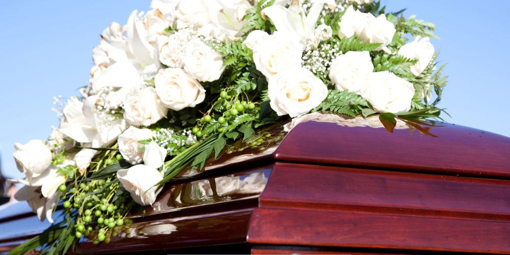 Polished wooden casket topped with white roses and greenery at an outdoor service by a Funeral Home and Cremations in Milwaukee, WI.