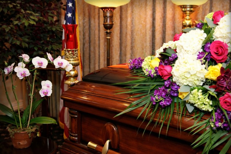 Wood casket with floral tribute at Long Beach, NY funeral home and cremations service with candles and flag